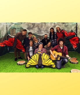 actors in plaid shirts holding giant butterfly puppets and guitar